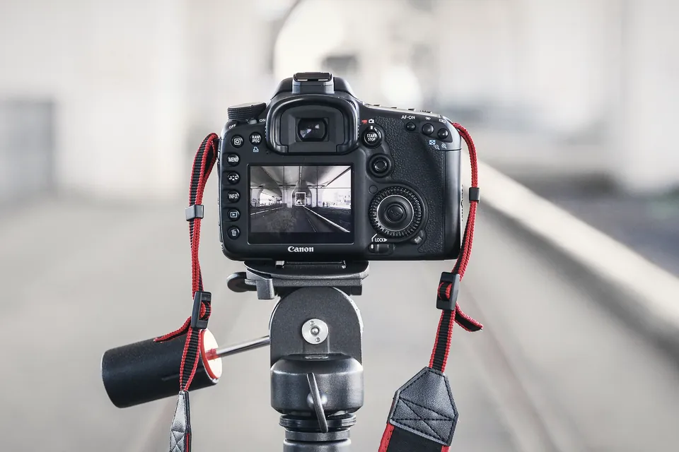 A camera on a tripod set up on a city street at dusk