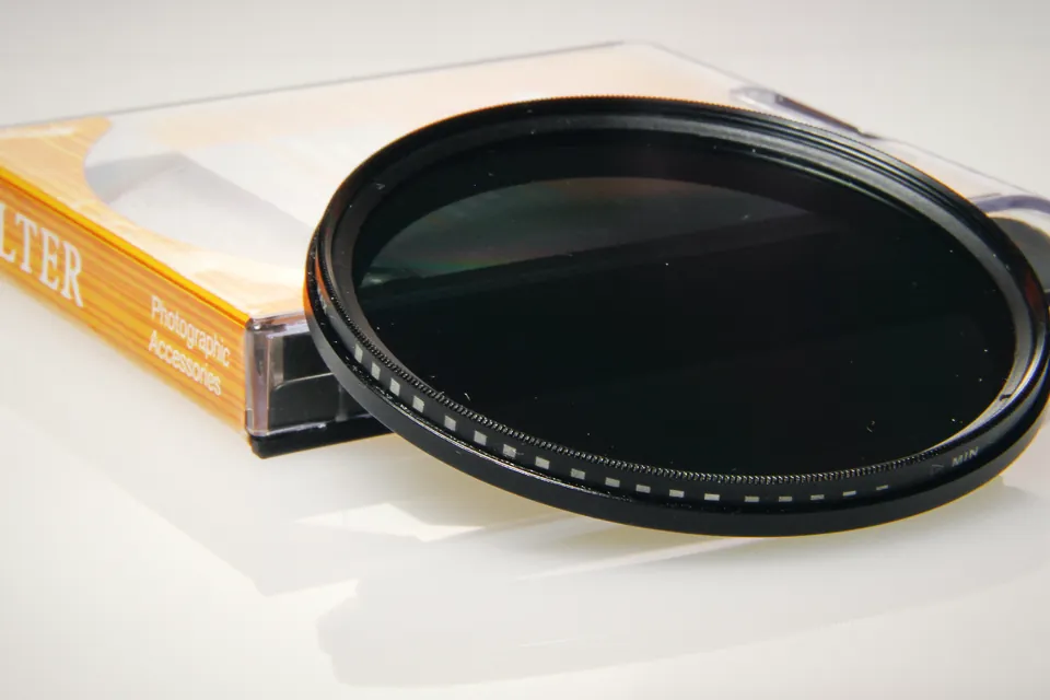 An unbranded variable ND filter with MIN marking and graduated dots on its front ring, leaning on its orange filter case