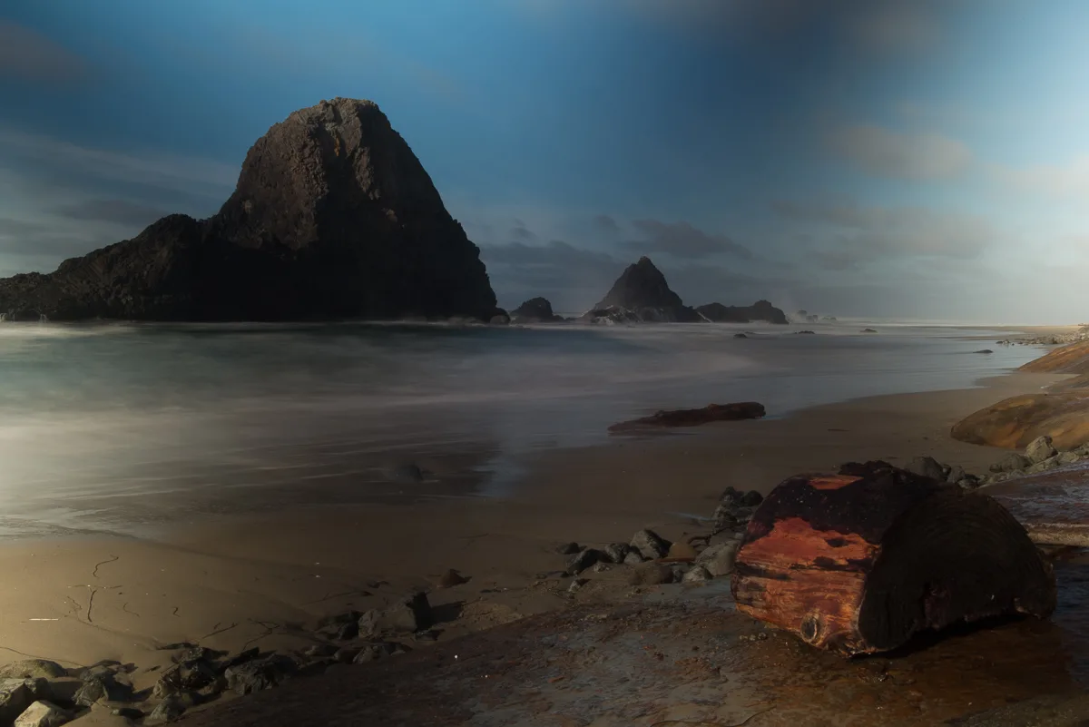 Long exposure of a rocky beach at dusk with dark, uneven blue bands across the sky caused by a variable ND filter turned close to its maximum